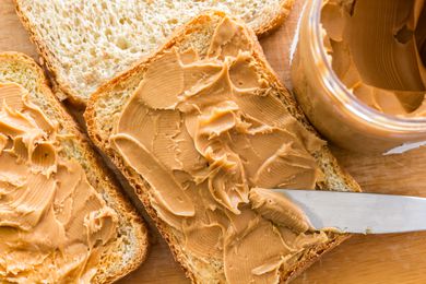 A peanut butter sandwich in progress, with peanut butter spread on a piece of bread by a butter knife