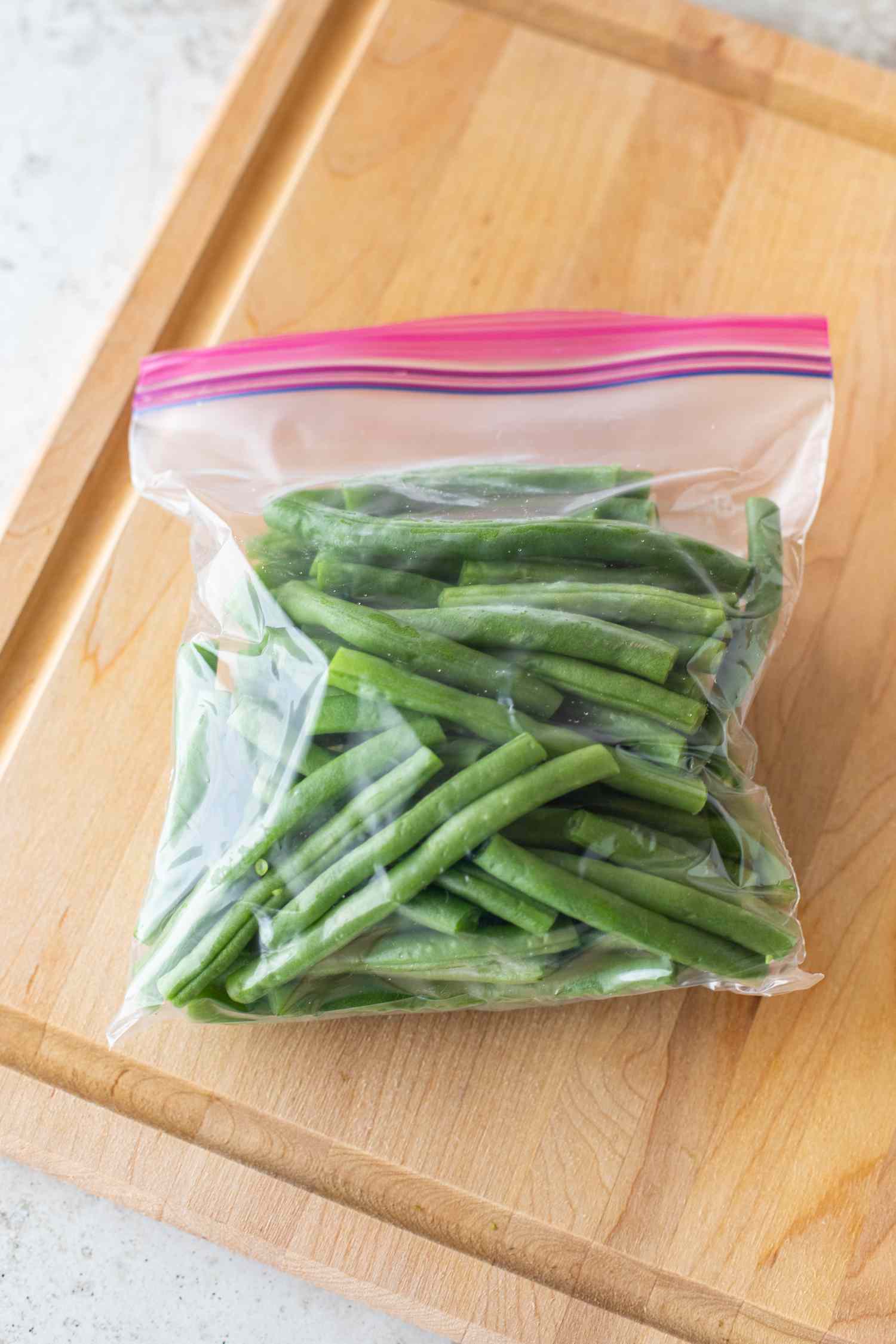 Bag of green beans on a wooden cutting board