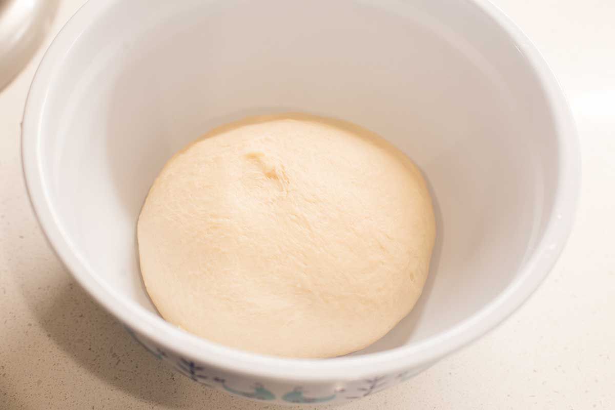 A ball of homemade beignet dough is in a white bowl on a counter.
