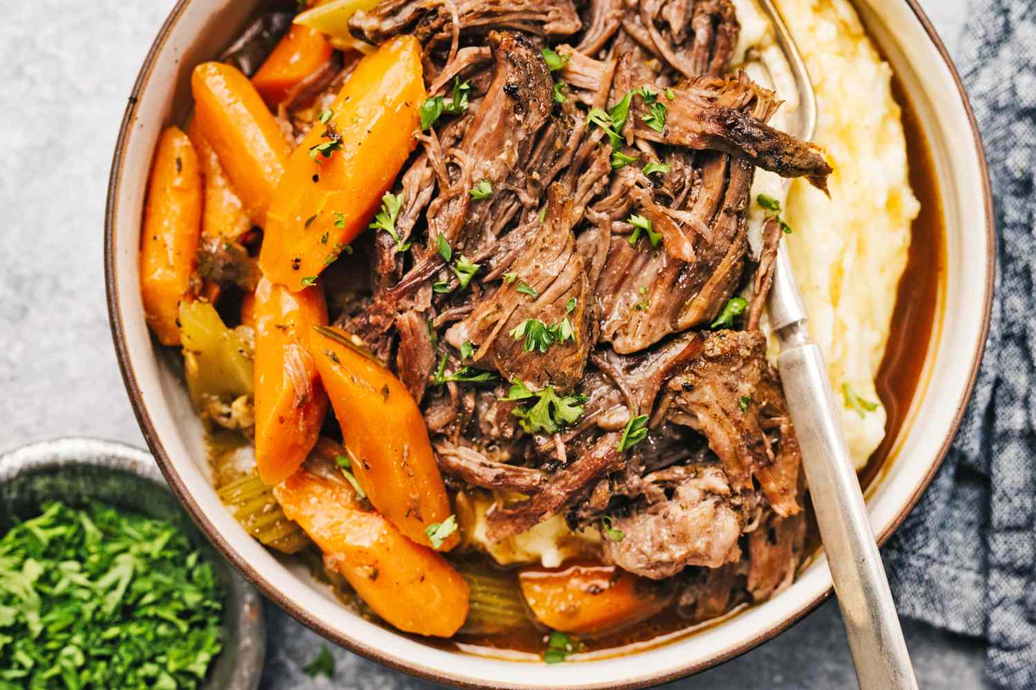 A bowl of pot roast with carrots and mashed potatoes