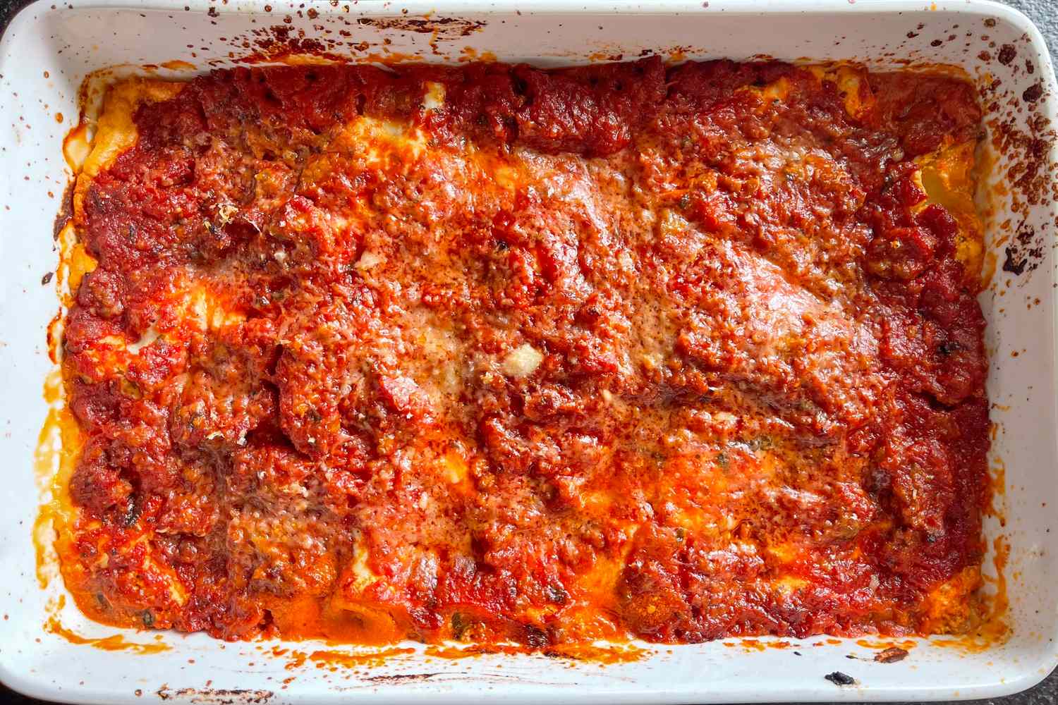 A baked lasagna with a layer of tomato sauce and melted cheese in a white rectangular dish