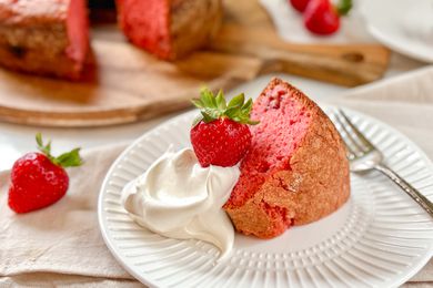 Slice of strawberry cake with whipped cream and a whole strawberry on a plate