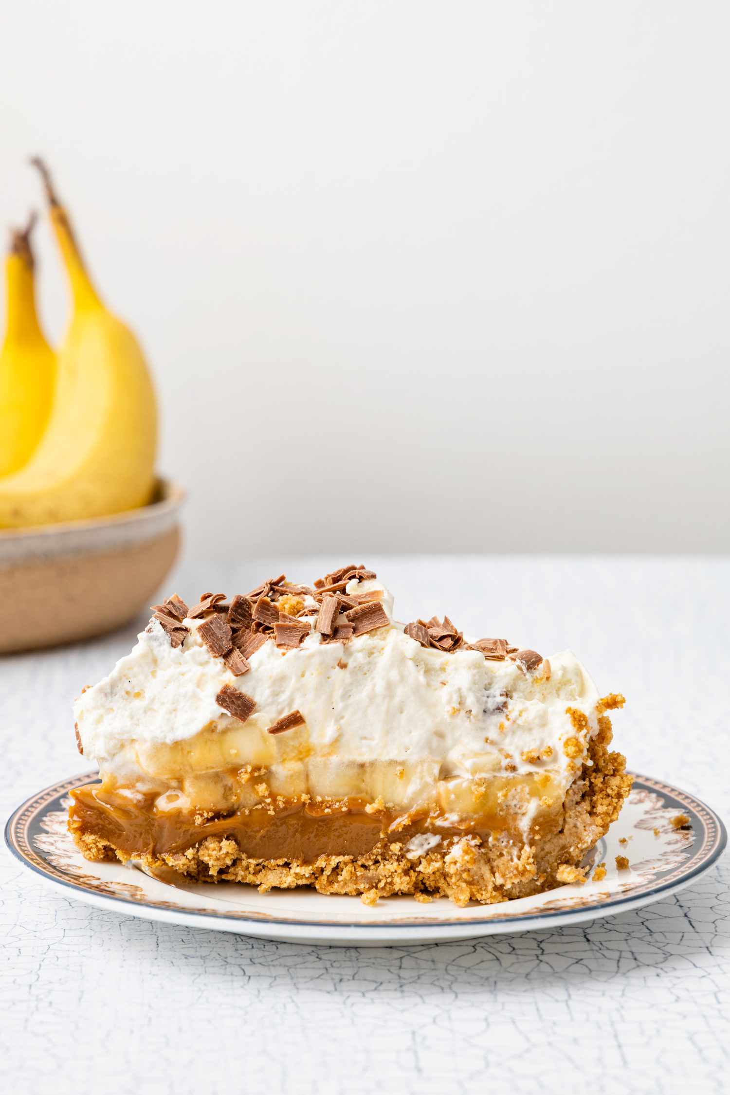 Slice of Banoffee Pie on a Small Plate, and in the Background, a Bowl of Bananas