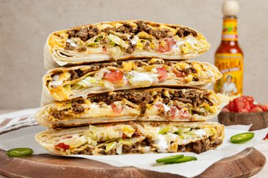Stack of Copycat Crunchwrap Supreme Cut in Half on Parchment Paper Over a Wooden Board