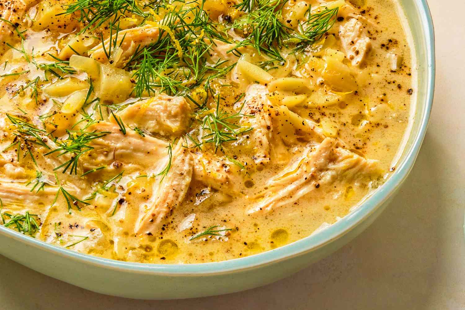 A closeup of a bowl of lemony orzo soup with herbs and visible chunks of meat and pasta