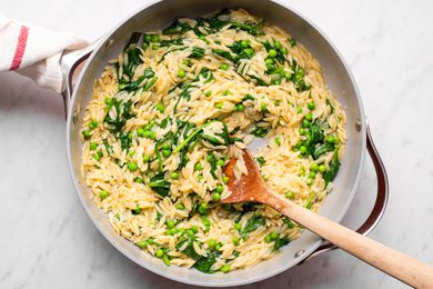 Orzo dish with greens and a wooden spoon in a pan