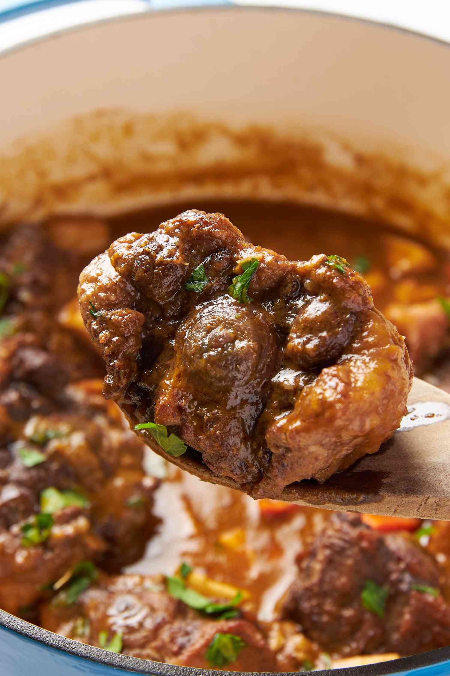 Close-up of a serving spoon with a braised oxtail scooped from a pot of oxtail stew