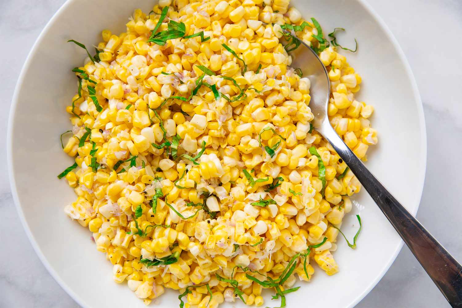Bowl of cold corn salad with herbs served with a spoon