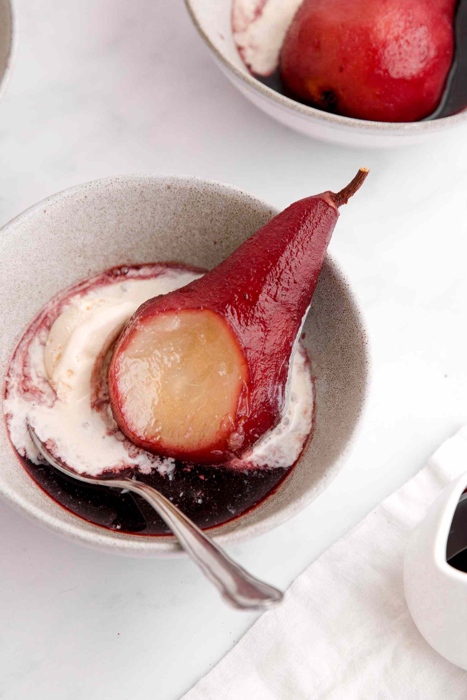 Red wine poached pear in white bowl with spoon.