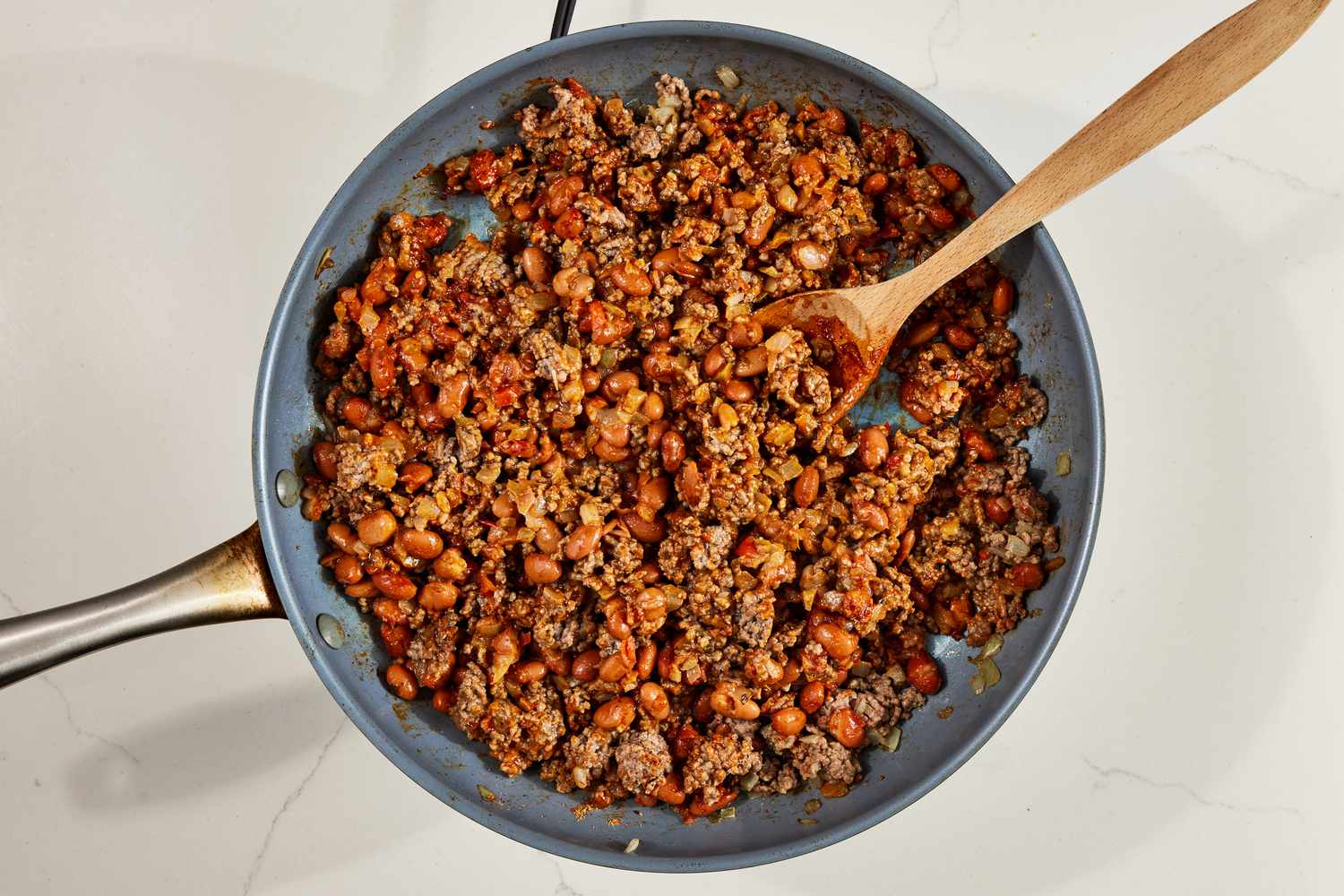 Beans and ground beef topping in a pan with a wooden spoon for walking tacos recipe