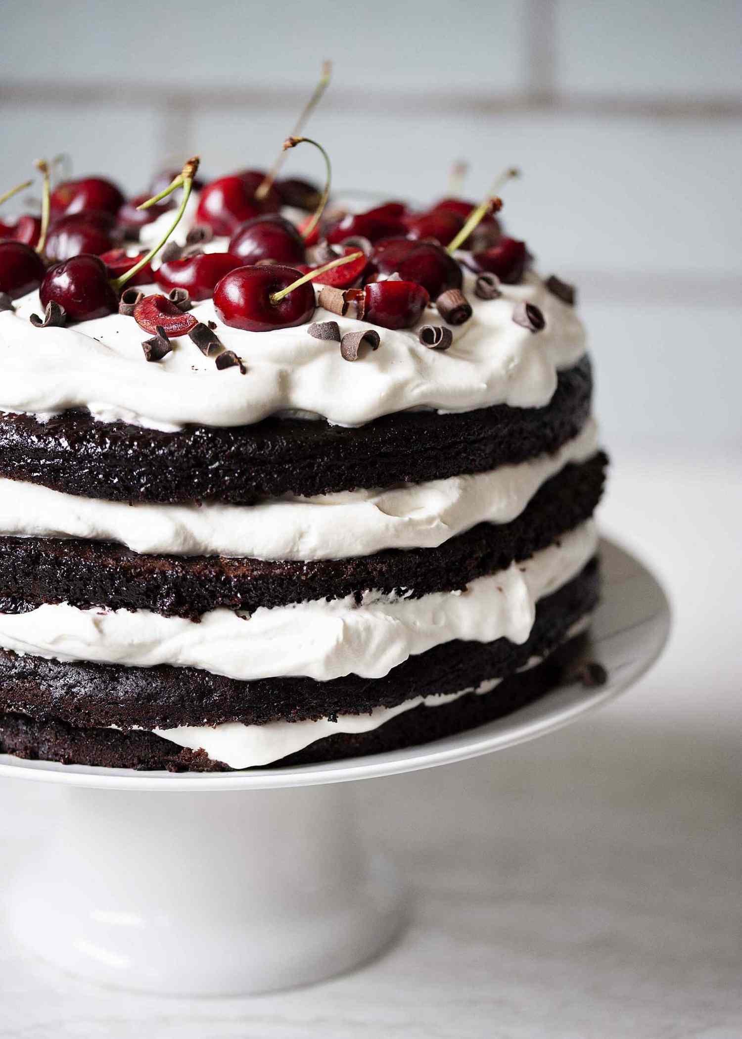 Authentic Black Forest Cake on a cake stand and topped with fresh cherries and chocolate.