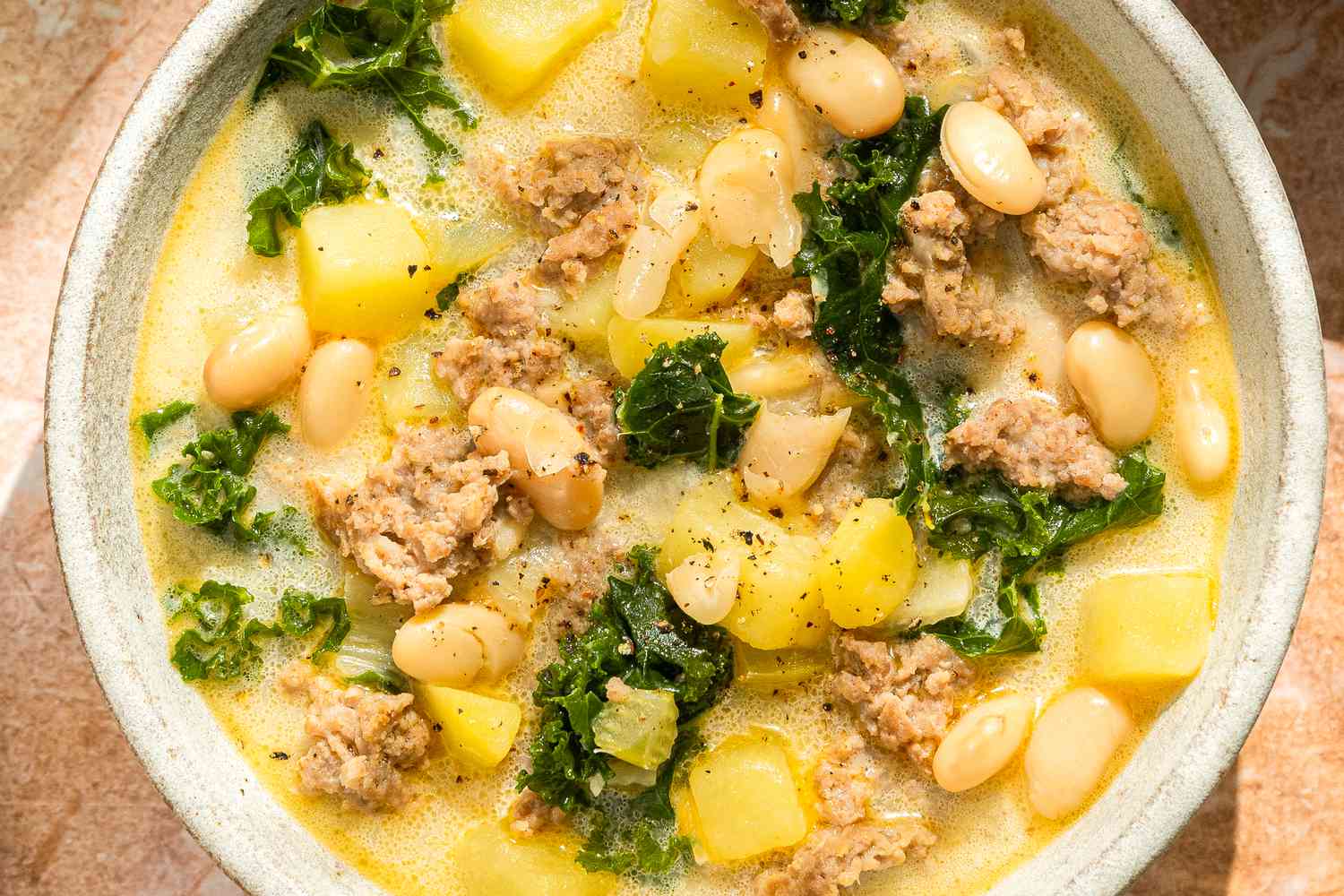 Overhead shot of a bowl with a cream based soup with beans, sausage, kale and potatoes
