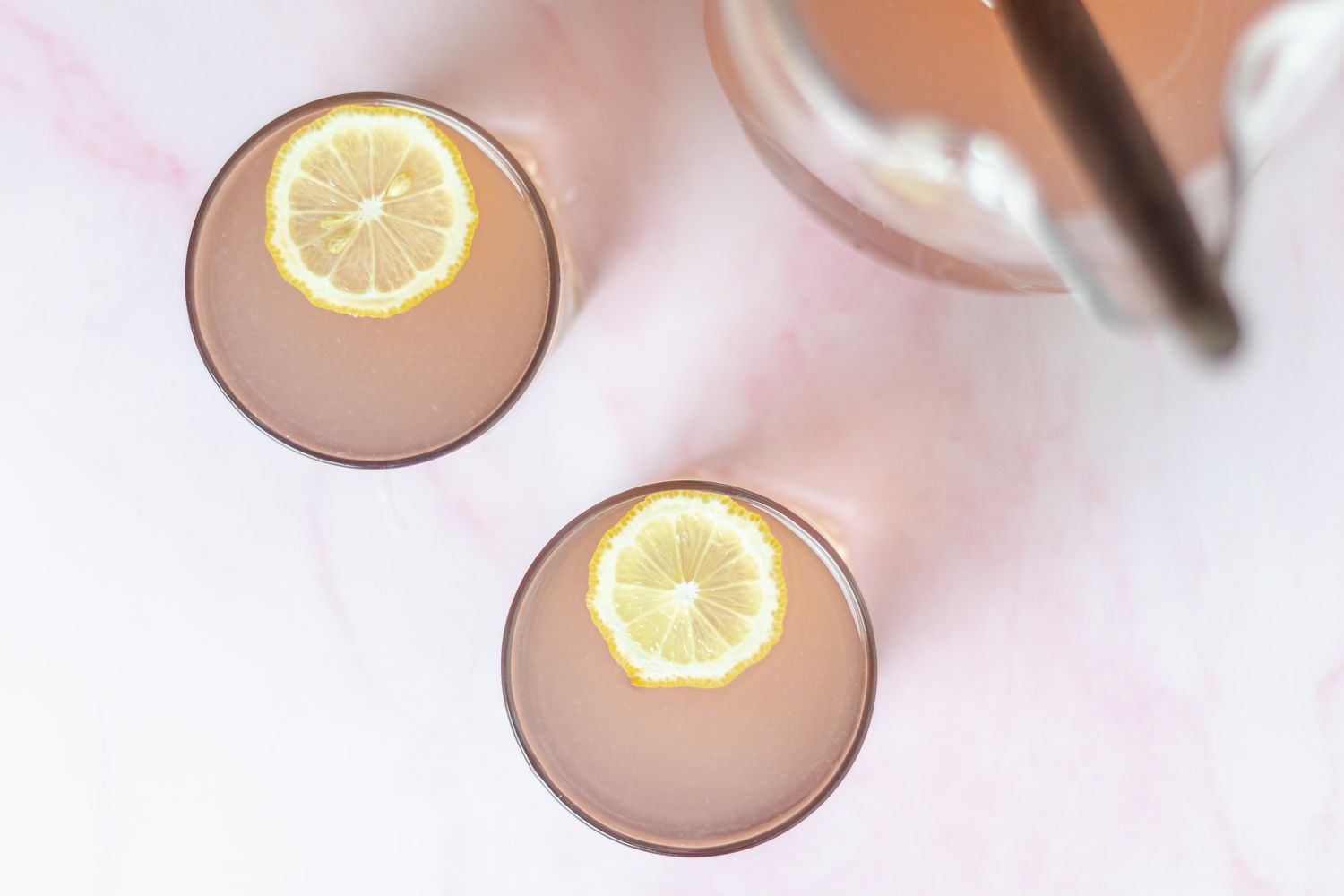 Overhead view of two glasses of pink lemonade garnished with lemon.