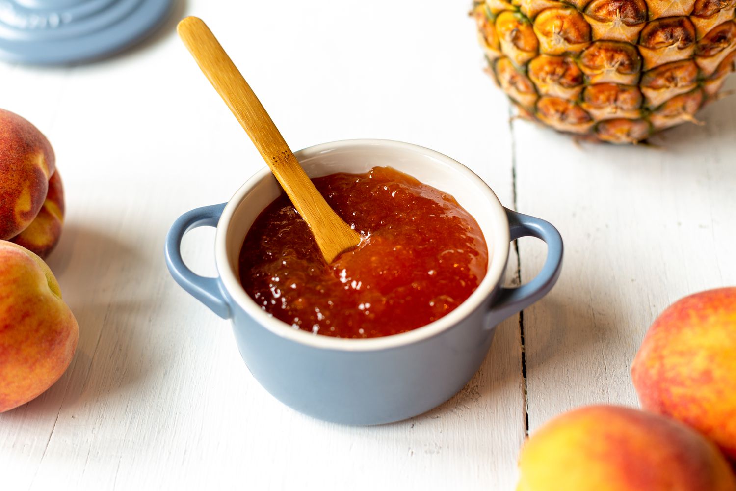 Peach and Pineapple Jam in a Small Dutch Oven Surrounded by Peaches and a Pineapple 