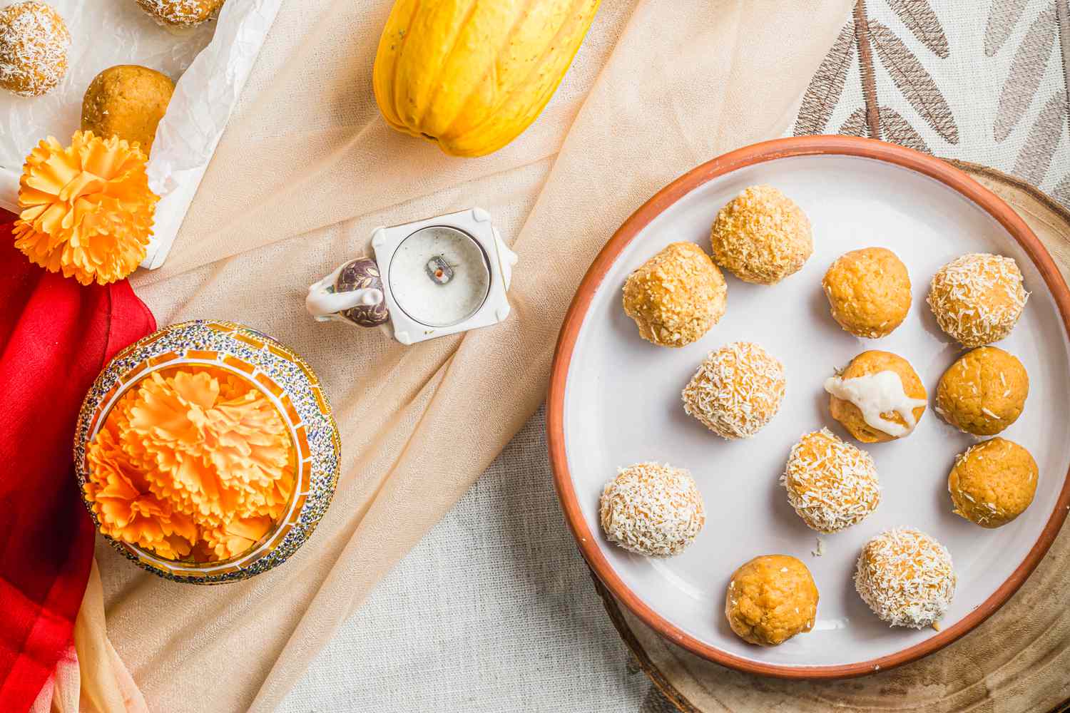 Pumpkin Ladoo on a Plate Next to a Candle Holder, an Ornate Jar with Flowers, and a Delicata Squash 