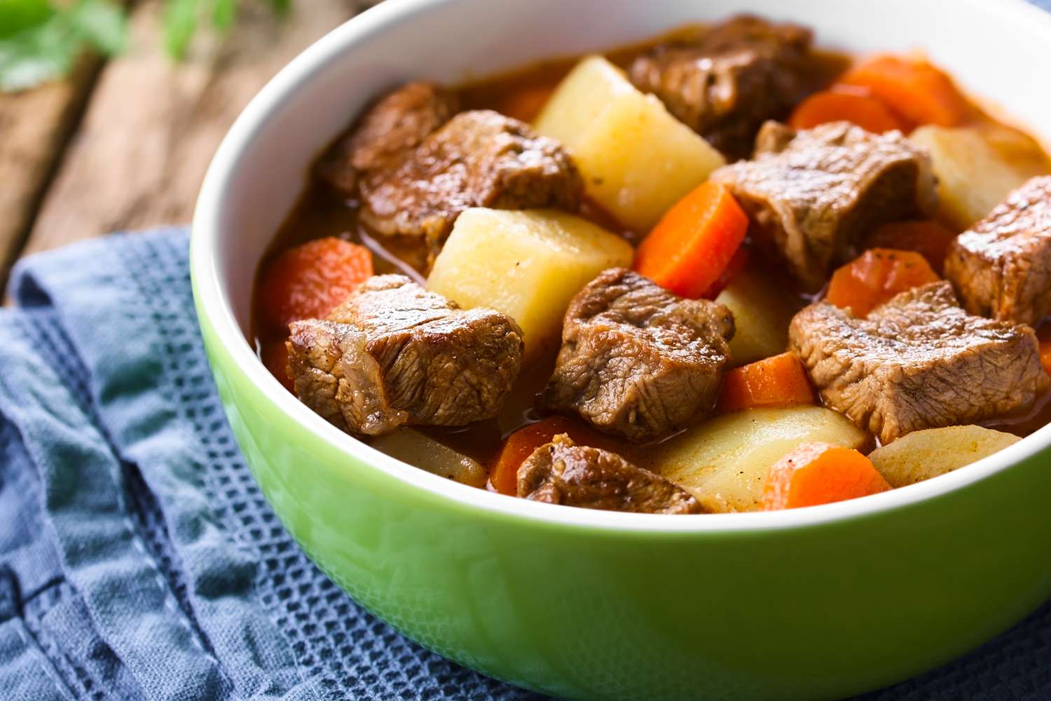A close-up of a bowl of beef stew showing chunks of tender beef, carrot rounds, and potato chunks