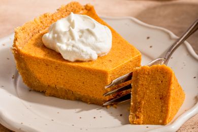 A slice of pumpkin pie with whipped cream on a plate a fork holding a small piece