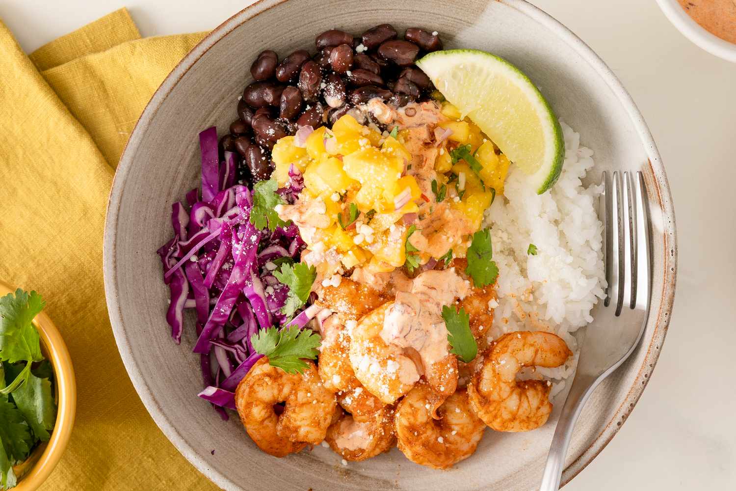 Cajun shrimp bowl with black beans, rice, purple cabbage, and mango salsa with a lime wedge