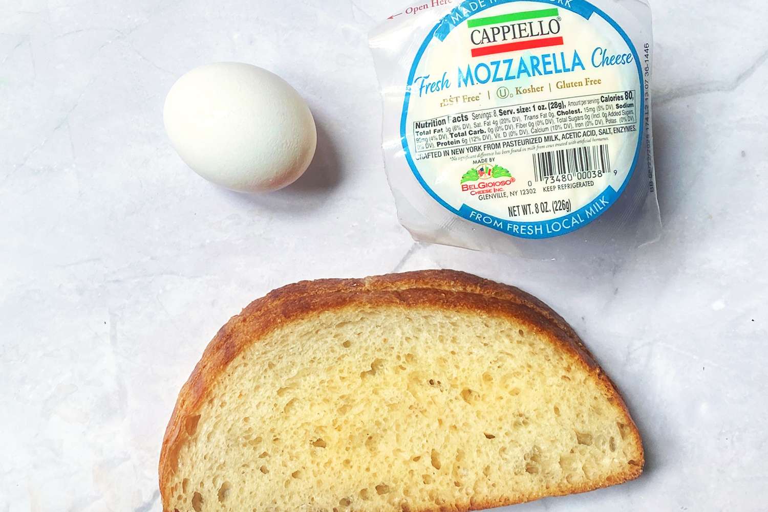 A slice of bread an egg and a package of fresh mozzarella cheese on a table