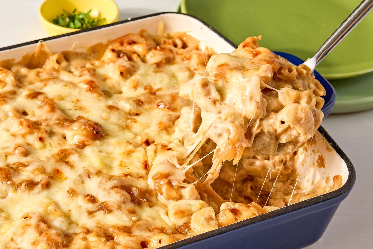 A casserole dish with cooked French onion mac and cheese some being lifted out with a serving utensil