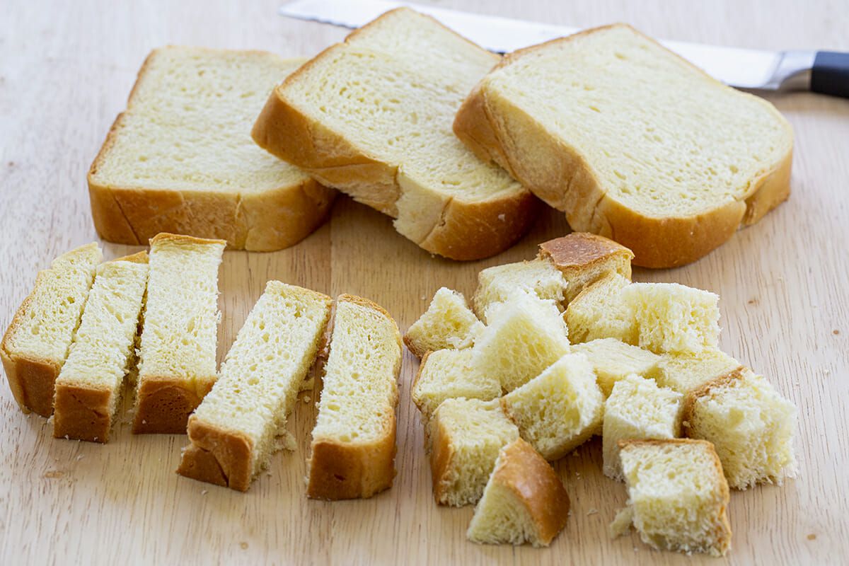 Bread slices cut into cubes and rectangles on a cutting board.