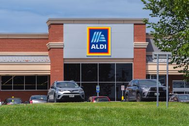 Front view of an Aldi store with cars parked in front featuring the logo prominently displayed on the building