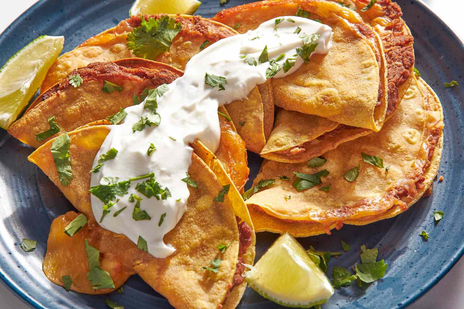Plateful of cheesy tacos topped with sour cream and cilantro 