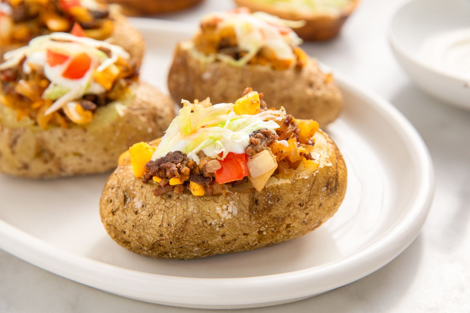 Baked potatoes topped with ground meat cheese and diced vegetables on a white plate