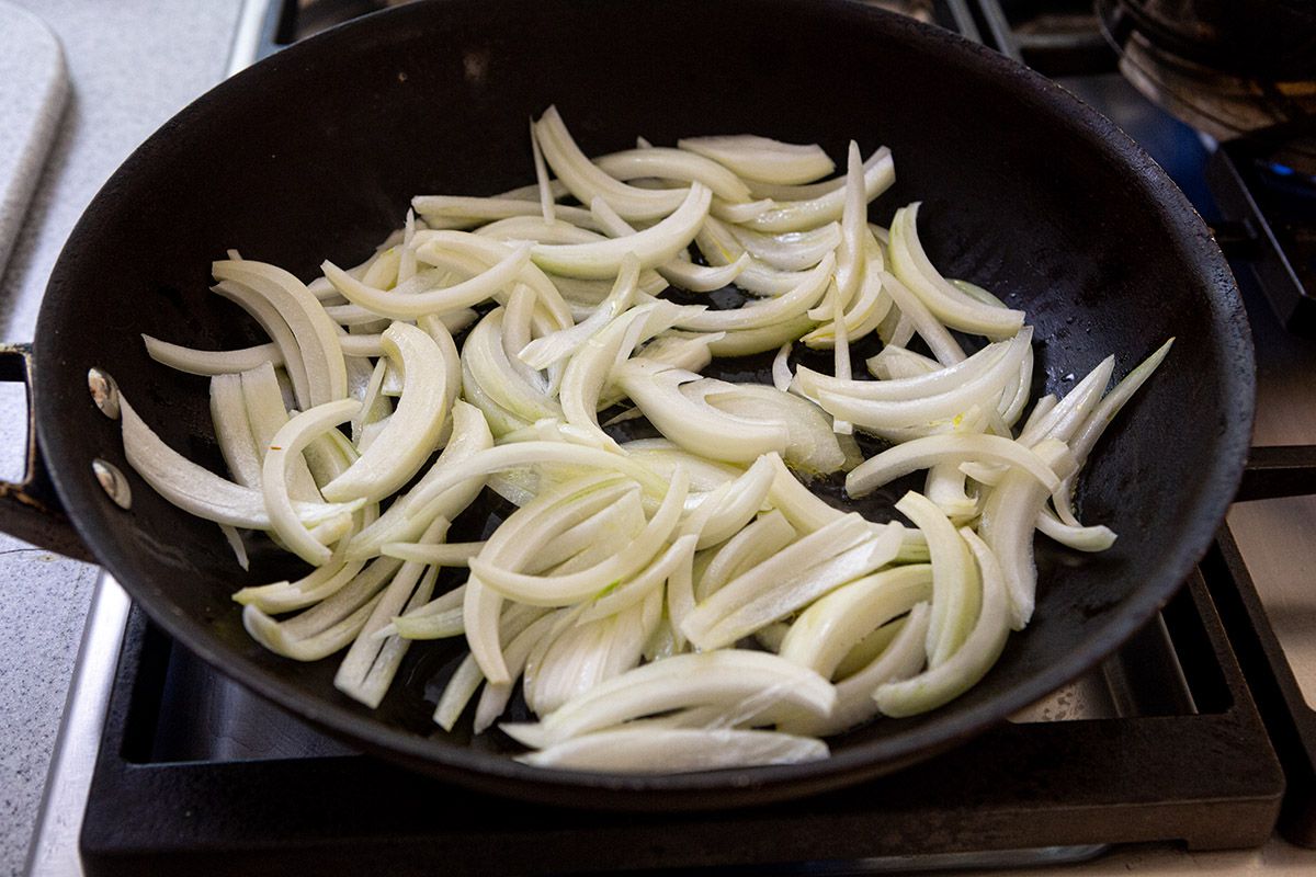 A skillet with sliced onions to make a broccoli rabe recipe.