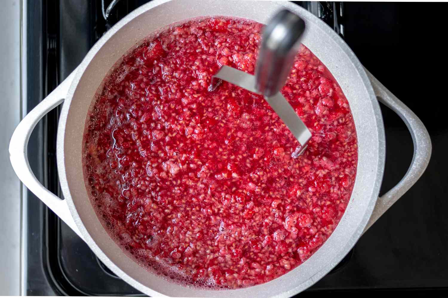 Mashing raspberries in a pot on the stove