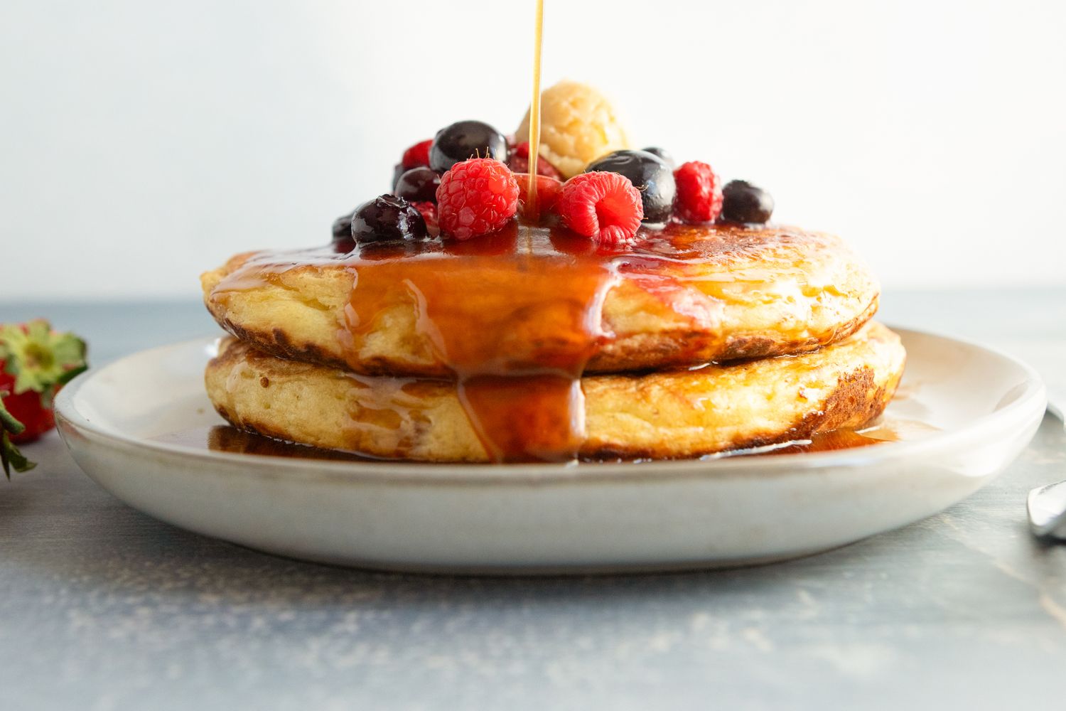 Stack of pancakes topped with syrup and fresh berries on a white plate