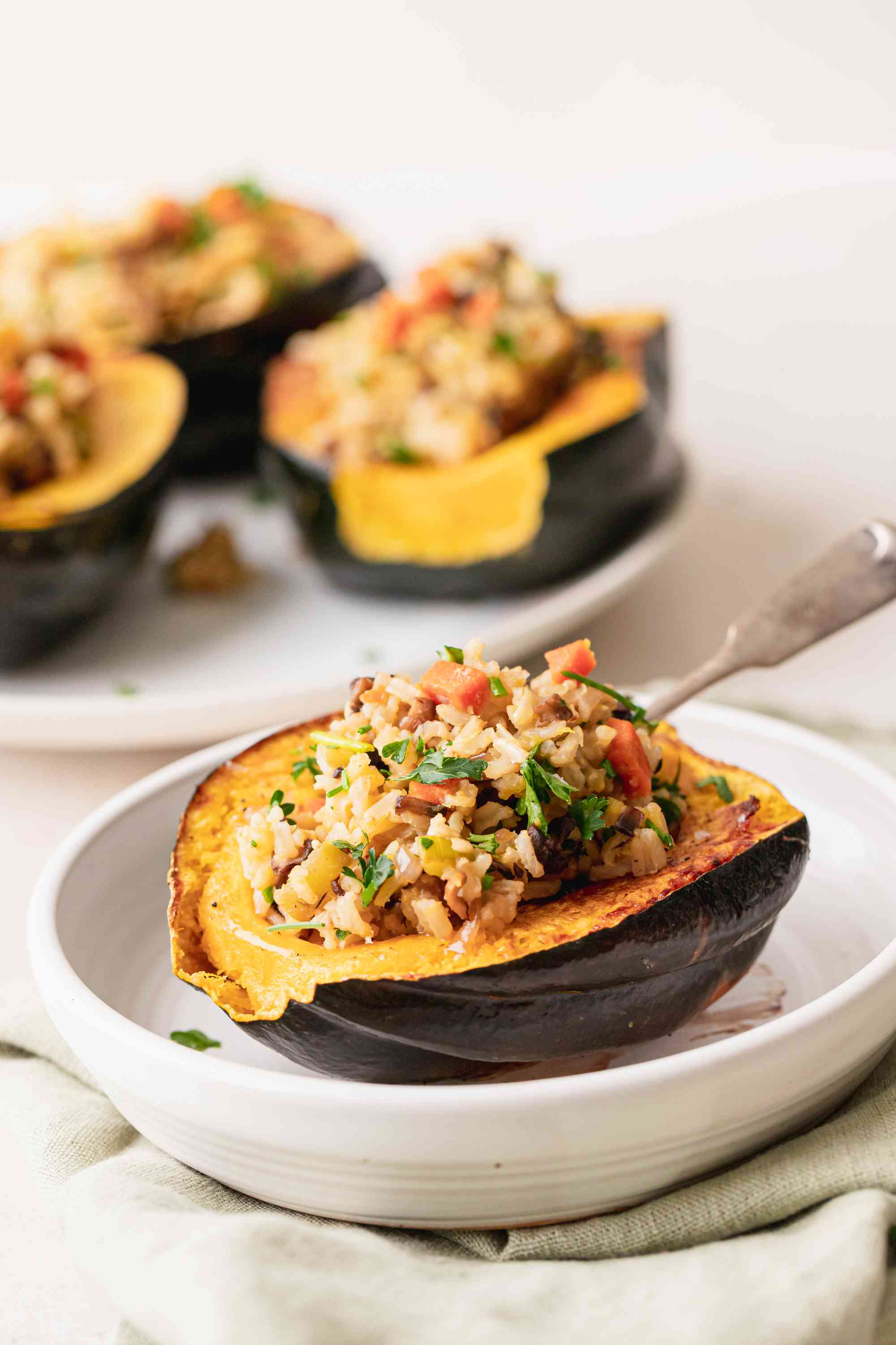 Side view of a vegan acorn squash in a low bowl and additional squash set behind it.