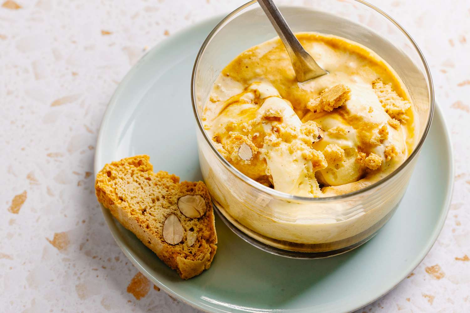 A glass dish of affogato with biscotti on the side on a lightcolored plate