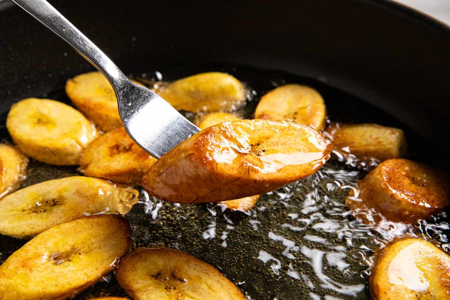 Fork Lifted a Fried Plantain From a Pot of Frying Oil With More Maduros