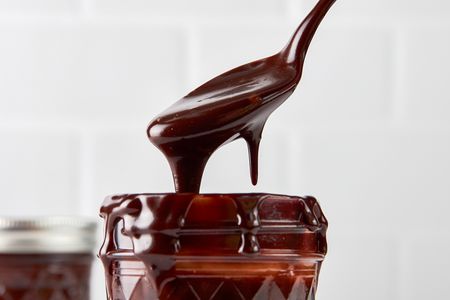 Hot fudge sauce cascading into a pint jar from a spoon 