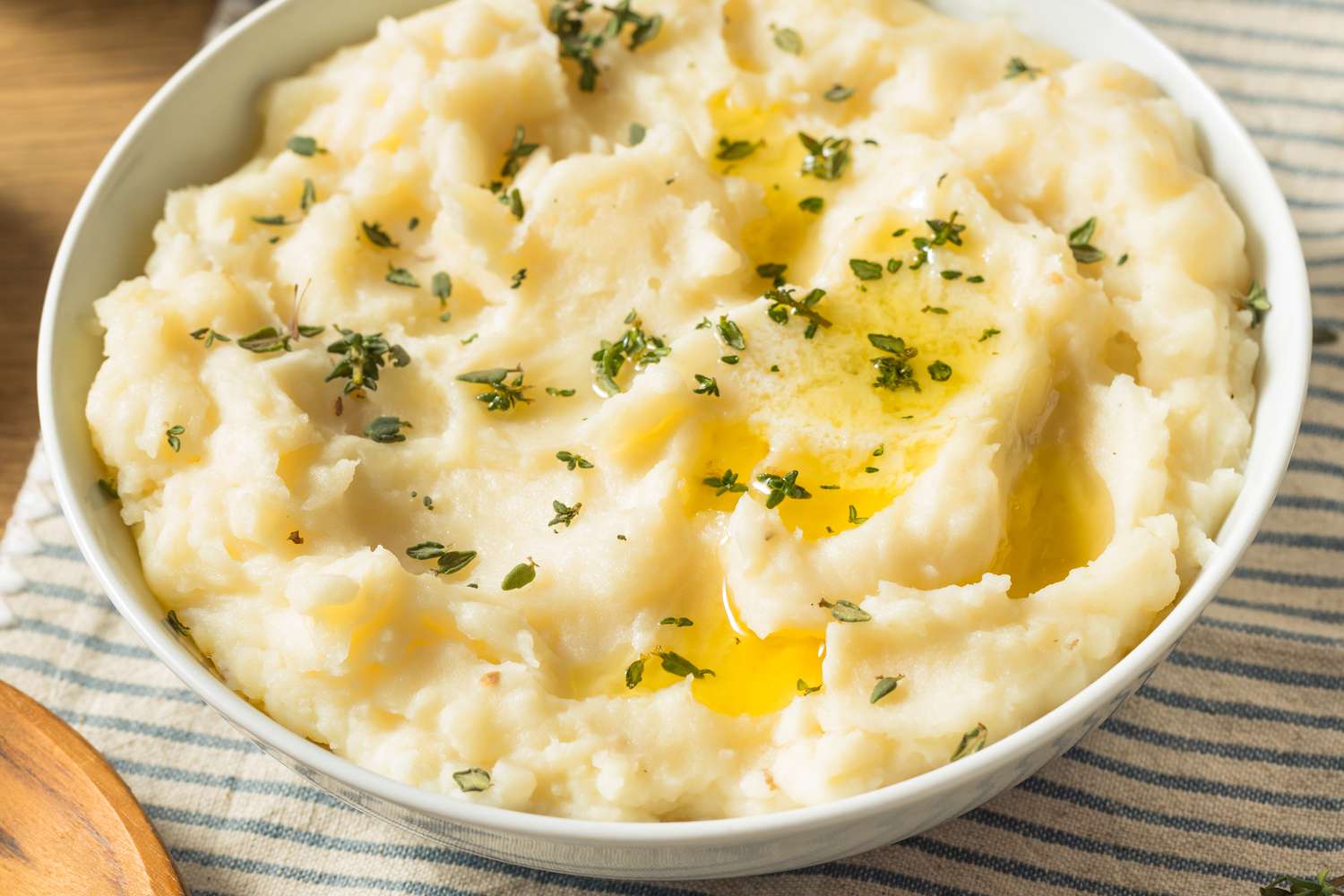 Angled view of a white bowl of mashed potatoes topped with butter and thyme