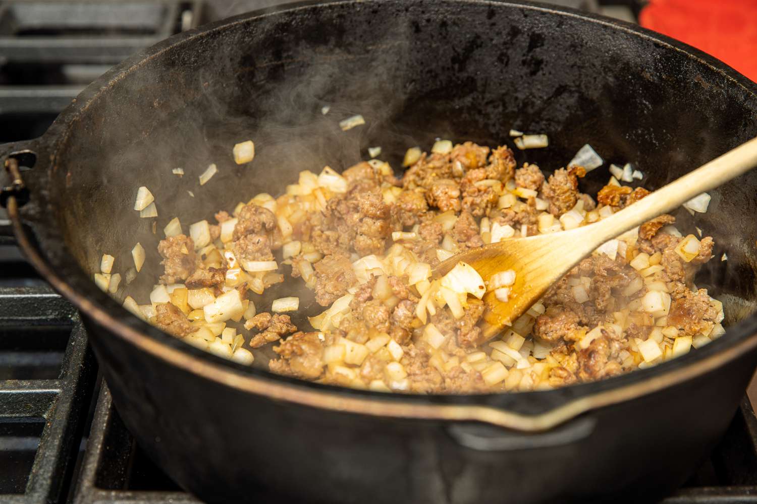 Sausage, Onions, and Garlic Cooking in a Cast Iron Pot and Mixed Using a Wooden Spoon