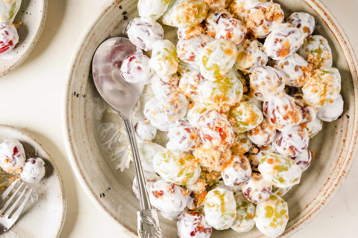 Bowl of grape salad with a spoon on the side topped with a creamy mixture and crumbled toppings