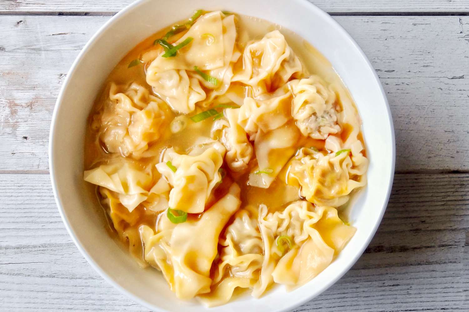 Overhead view of a bowl of pork and ginger wontons in chicken soup.