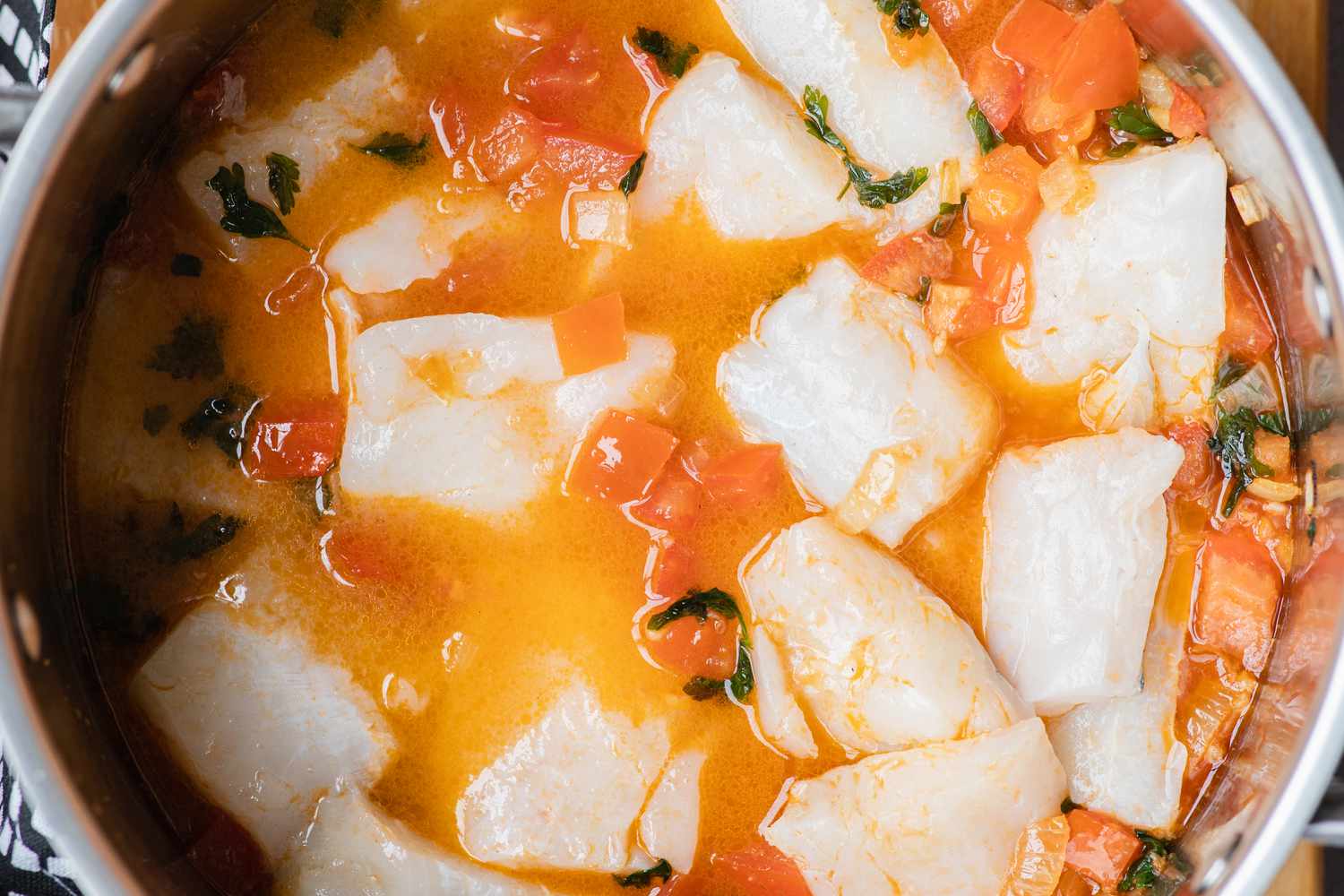 Adding fish and stock to vegetables for a seafood stew recipe.