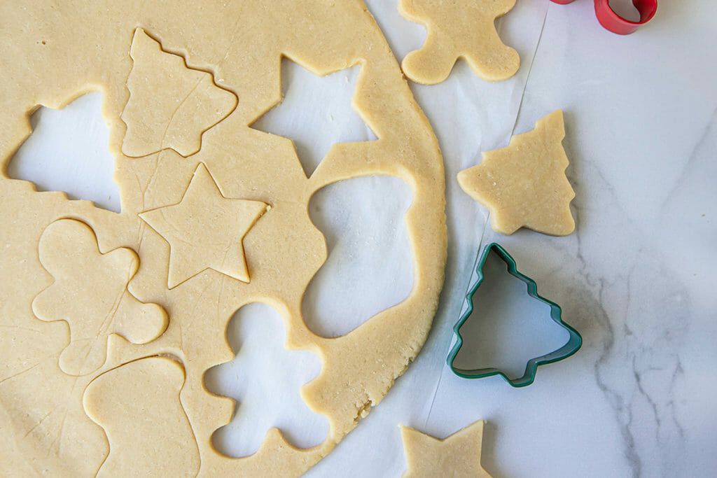 Dough for Christmas sugar cookies is rolled on a counter with shapes cut out.