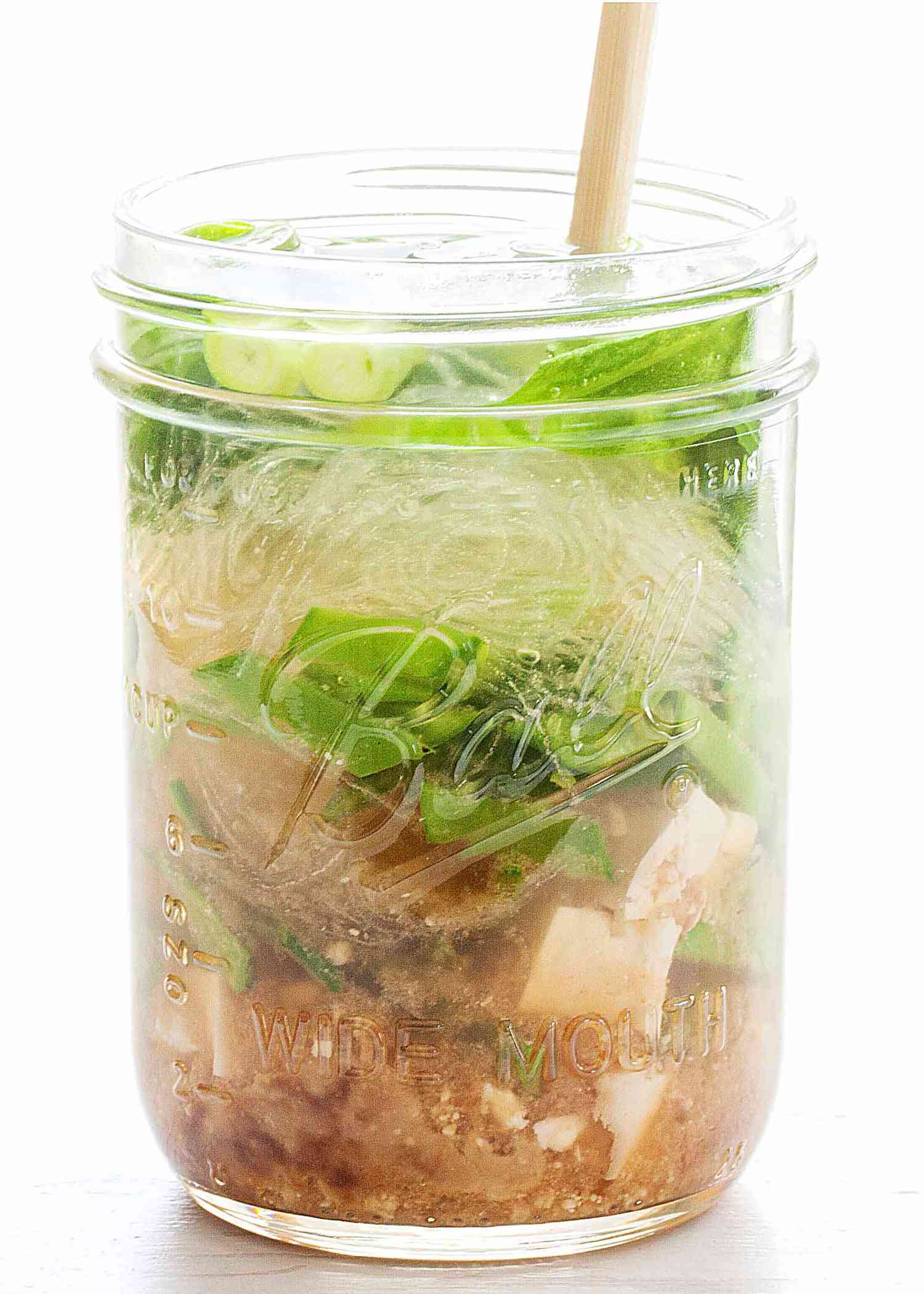 Mason jar filled with layered vegetables tofu and noodles prepped for a meal