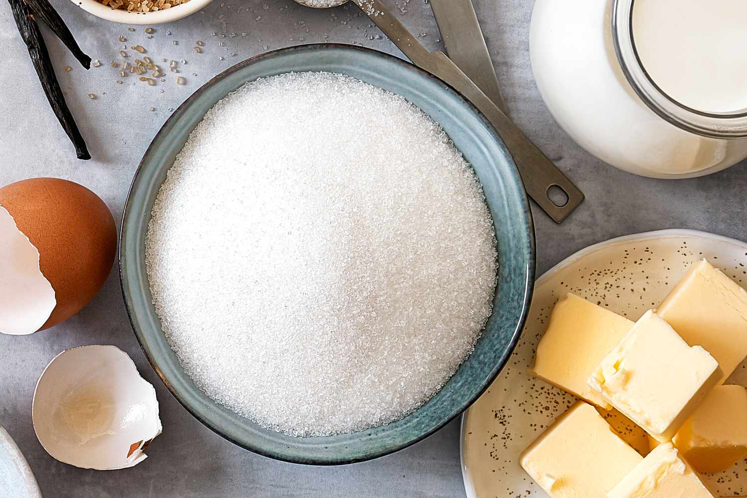 Baking ingredients: flour, eggs, sugar, butter, milk and spices on gray marble background.