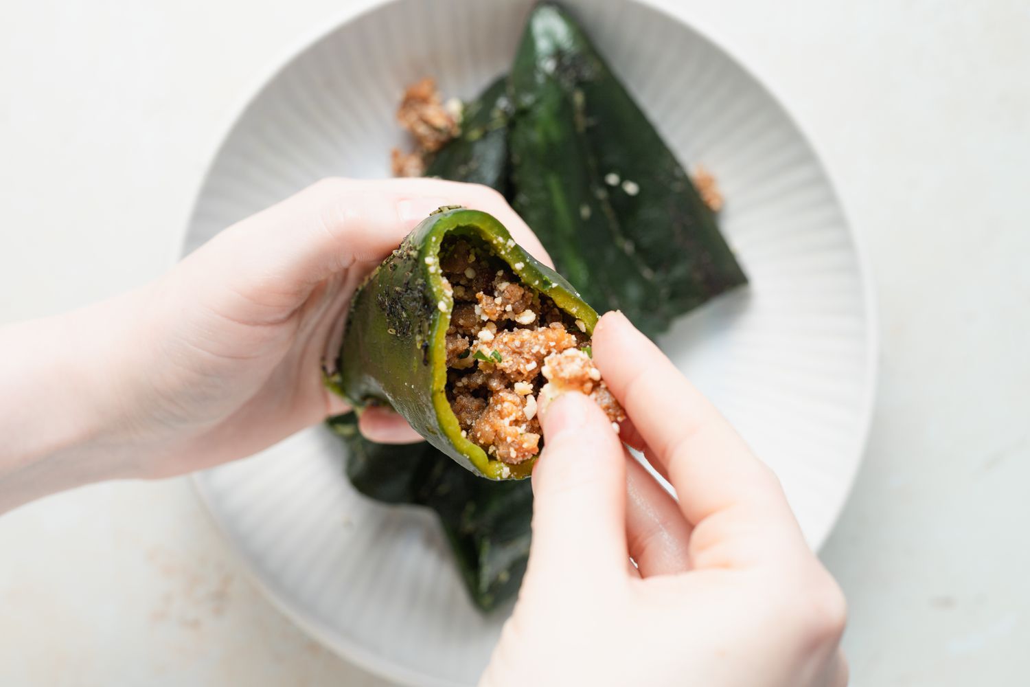 Hands stuffing chili peppers for a chili relleno casserole.