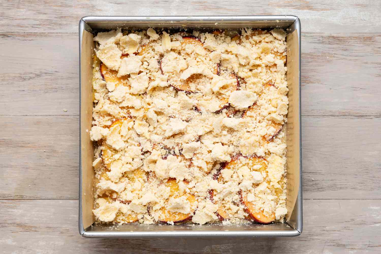crumbly topping over peach pie bars before baking
