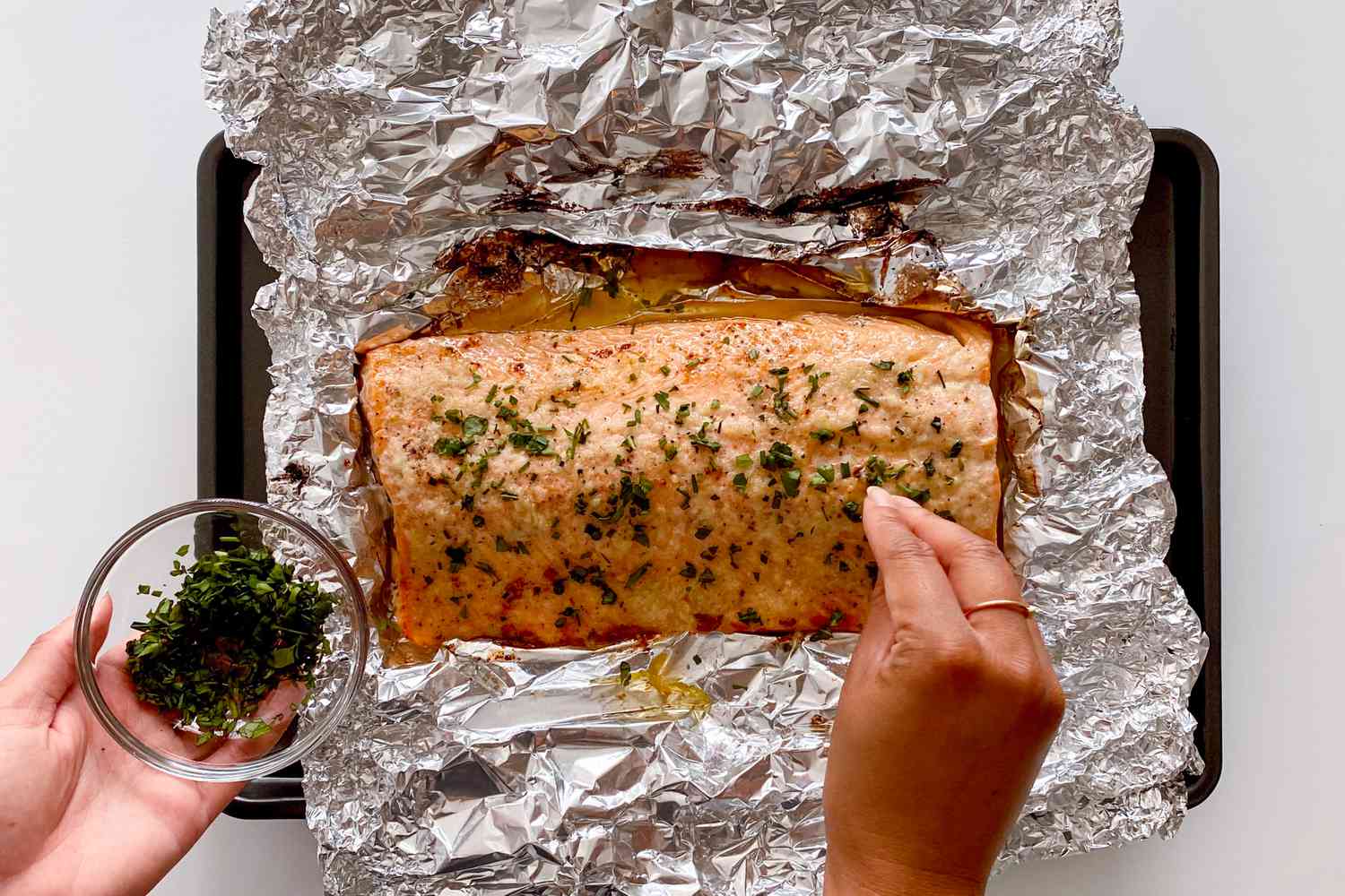 Sprinkling herbs on Honey Garlic Butter Roasted Salmon.