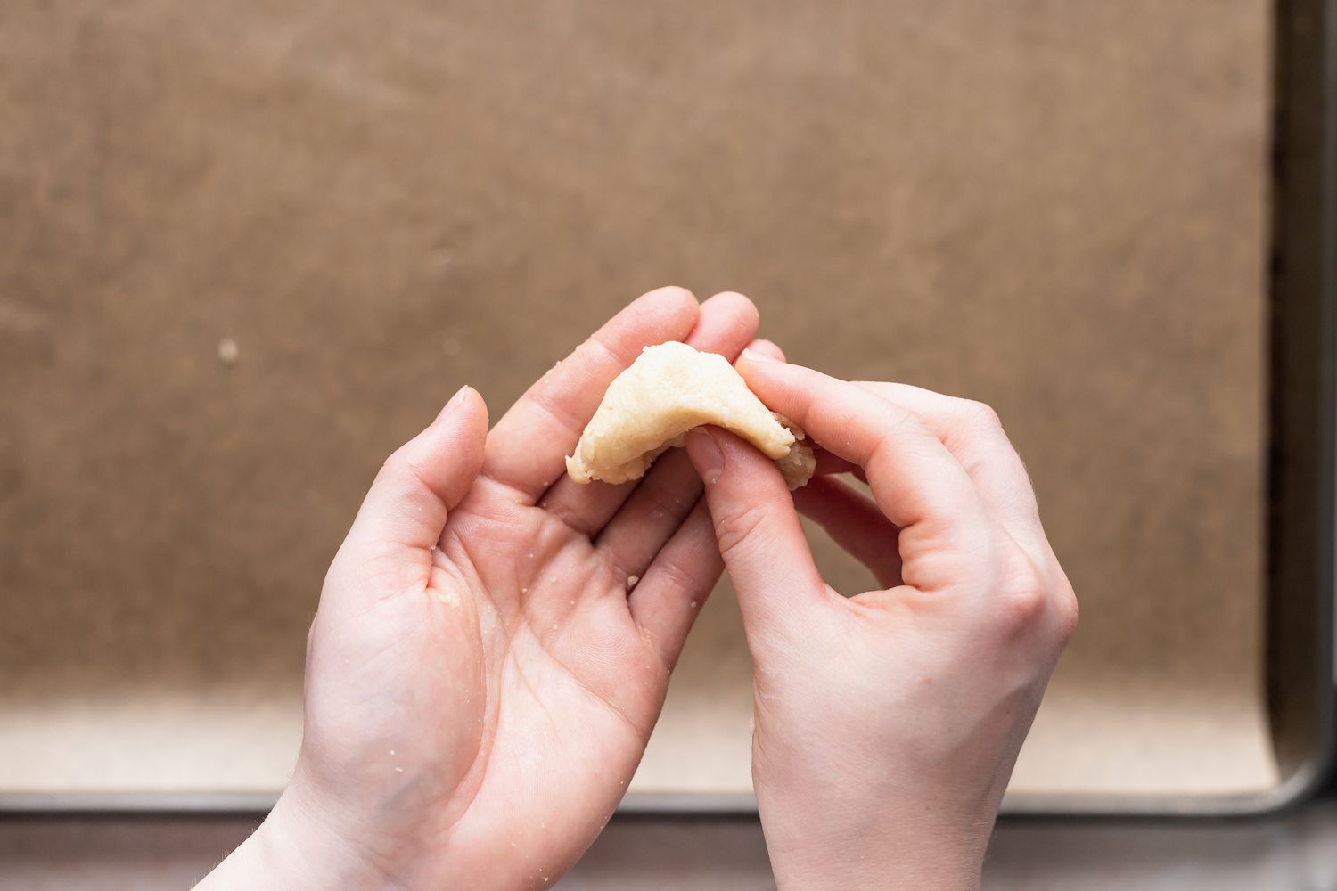 Shaping almond flour sugar cookies over a baking sheet covered in parchment.