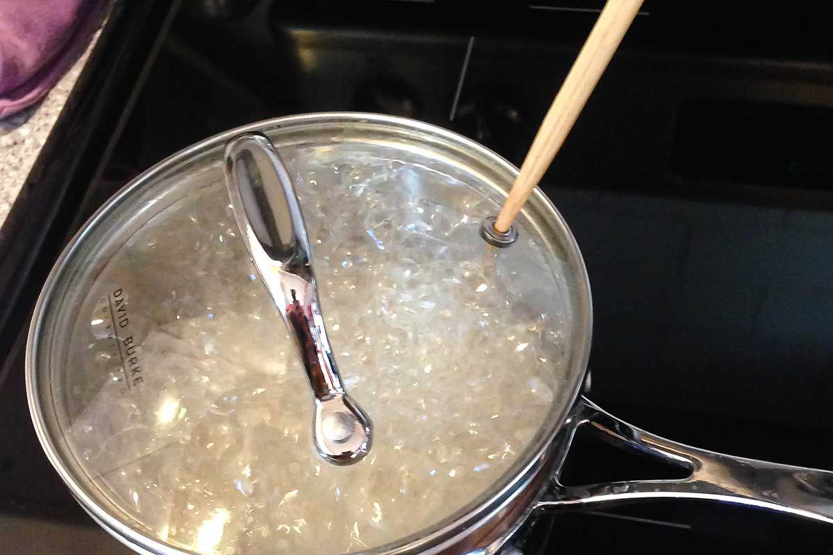 Long grain brown rice boiling in a pot with lid over pot