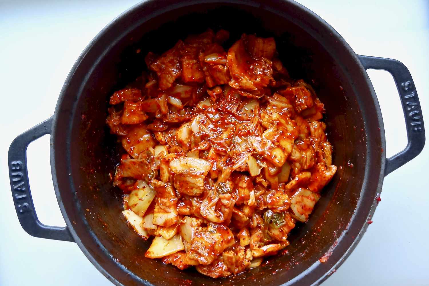 Overhead view of a dutch oven with ingredients mixed together for spicy kimchi and pork belly stew.