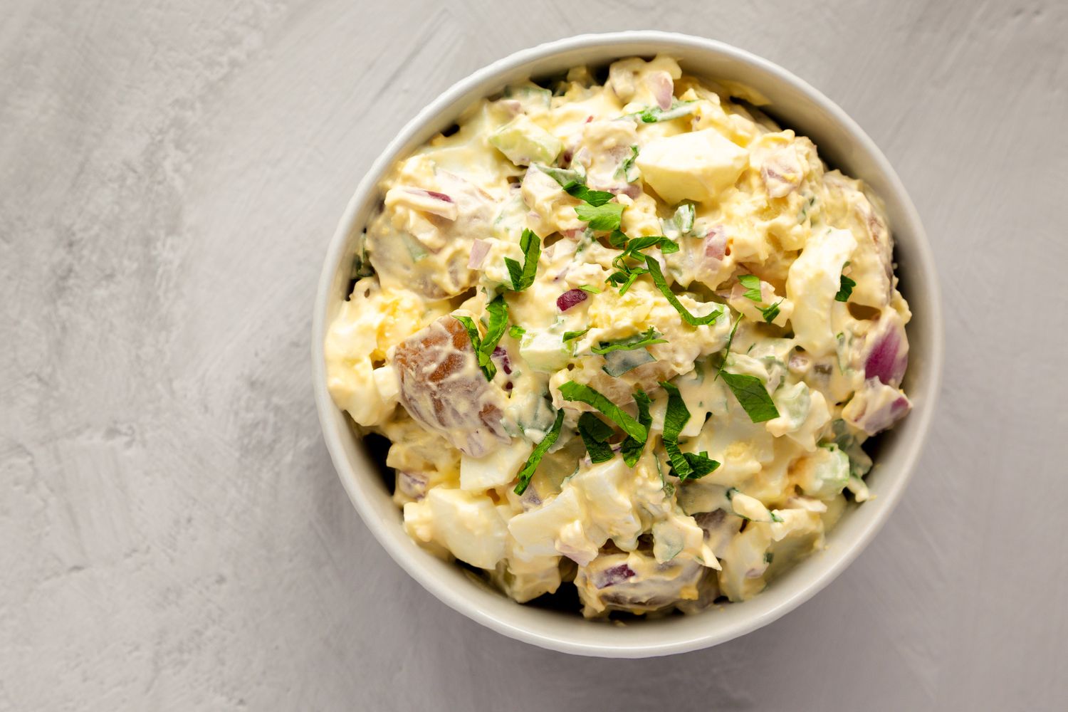 A bowl of creamy potato salad garnished with parsley
